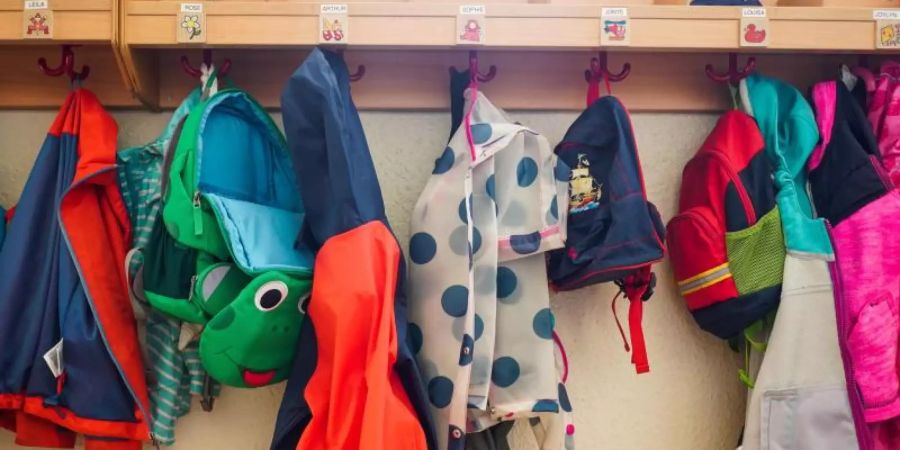 Jacken und Rucksäcke hängen an der Garderobe einer Kita. (Symbolbild). Foto: Jörg Carstensen/dpa