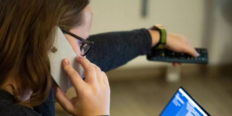 Eine Frau bedient beim Telefonieren einen Fernseher, vor ihr steht ein aufgeklappter Laptop. Neuen Hinweisen zufolge sind Frauen nicht generell besser beim Multitasking als Männer. Foto: Lino Mirgeler/Symbolbild