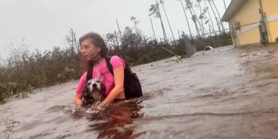 Julia Aylen watet mit ihrem Hund durch hüfthohes Wasser auf einer überfluteten Strasse.