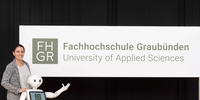 Digital-Business-Management-Studentin Mara Carl und Pepper praesentieren das Logo der FH Graubuenden. FH
