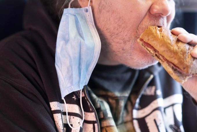 Ein Mann mit einer Hygiene Einwegschutzmaske am Ohr, isst im SBB-Zug von Bern nach Brig einen Sandwich, Coronavirus Maske SBB essen