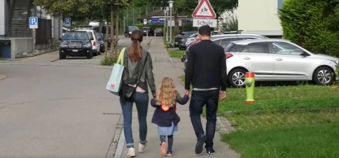 Ein Kind wird auf dem Schulweg von seinen Eltern begleitet. Schule