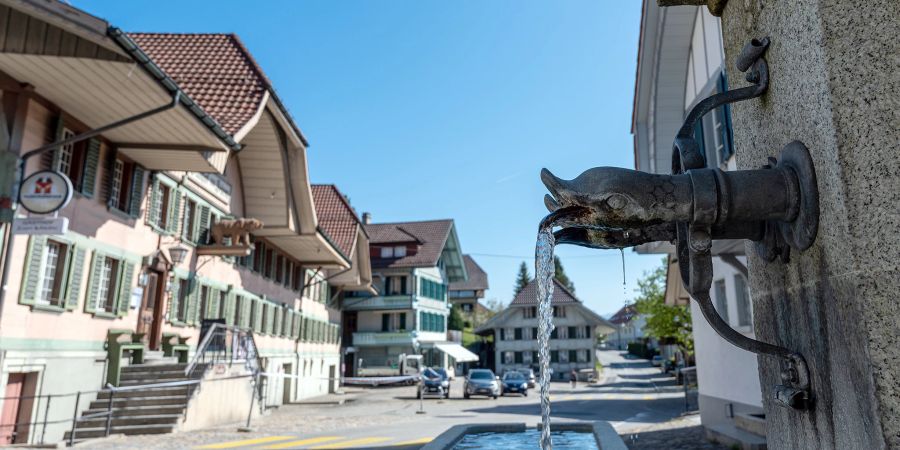 Ein Brunnen und hinten links der Gasthof Bären im Dorfzentrum von Signau.