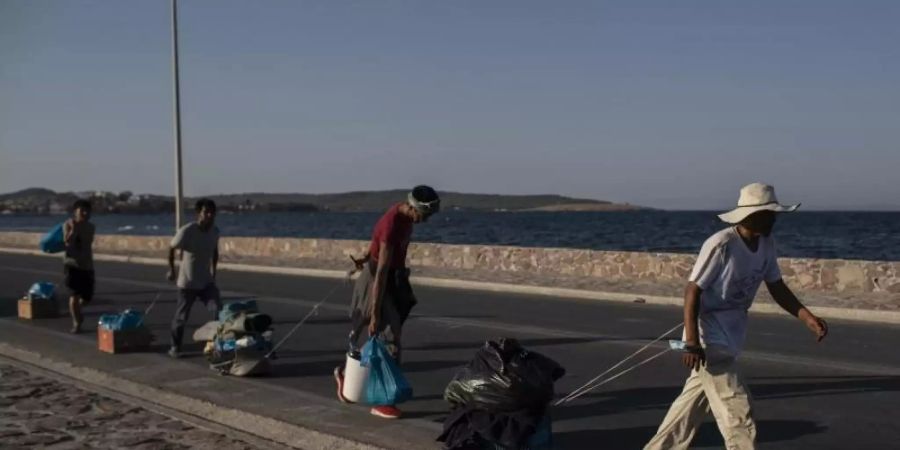 Flüchtlinge auf Lesbos ziehen ihre Habseligkeiten hinter sich her. Foto: Petros Giannakouris/AP/dpa