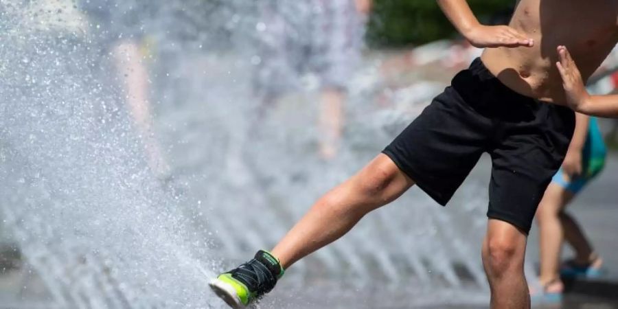 Ein Junge spielt am Stachus in München mit dem Wasser von einem Brunnen. Foto: Sven Hoppe/dpa