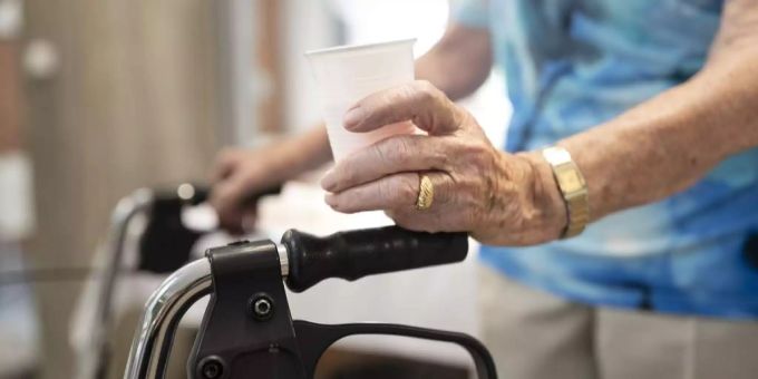 Eine betagte Person mit Gehhilfe und Plastikbecher, Altersheim Betagtenheim Senior