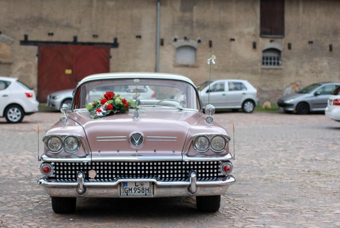 Oldtimer sind als Hochzeitsautos beliebt. Oldtimer Chamoagner Blumenschmuck Platz Kopfsteinpflaster