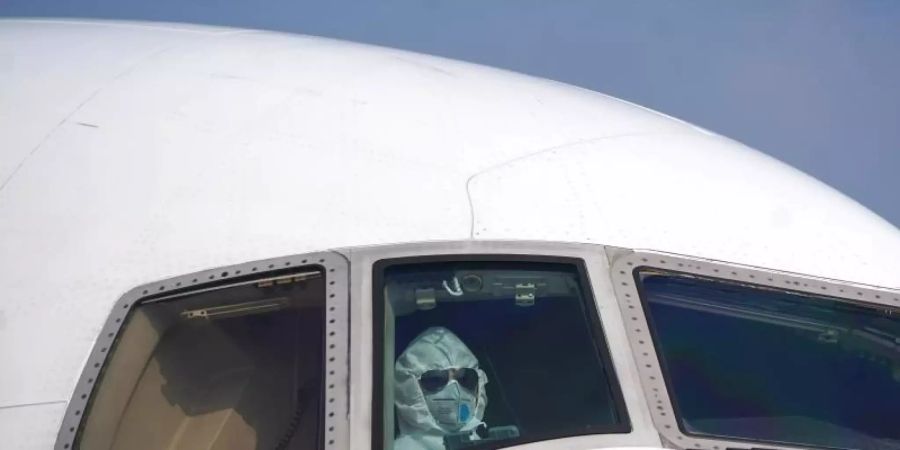 Ein Pilot sitzt mit Schutzanzug und Maske im Cockpit und parkt ein Flugzeug auf dem Internationalen Flughafen Wuhan-Tianhe. Foto: Cheng Min/XinHua/dpa