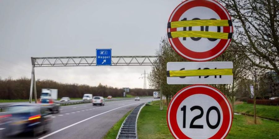 Ein Verkehrsschild mit Tempo 100 ist an einer Autobahn in Meppel über einem Schild mit dem Tempolimit 120 angebracht, aber noch überklebt. Im Kampf gegen gefährliche Stickoxide beginnen die Niederlande mit der Einführung von Tempo 100 auf Autobahnen. Foto: "wilbert Bijzitter"/ANP/dpa