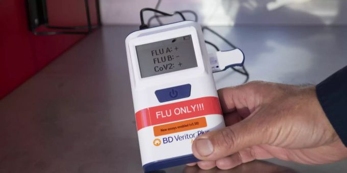 Ein Mann zeigt ein Gerät, dass gleichzeitig auf das Coronavirus und Influenza testet. Coronavirus Flurona