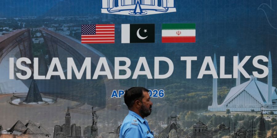 Ein Polizeibeamter geht vor einem Medienzentrum an einer Plakatwand zu den Verhandlungen zwischen den USA und dem Iran vorbei. Foto: Anjum Naveed/AP/dpa