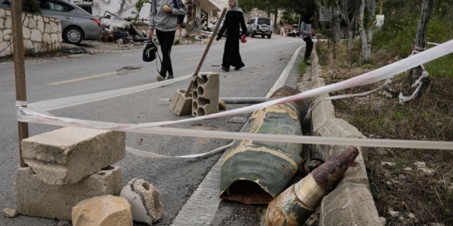 Menschen gehen neben Raketenteilen im Dorf Halloussiyeh im Südlibanon vorbei. Foto: Bilal Hussein/AP/dpa