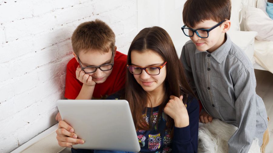 drei kinder schauen mit brille auf pad