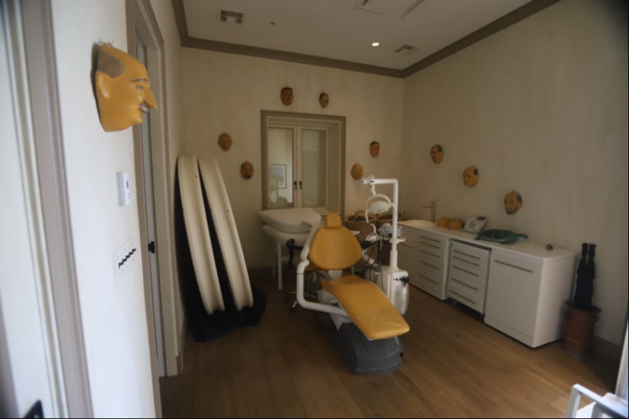 In einem Zimmer steht ein alter Zahnarztstuhl, an den Wänden hängen Masken.