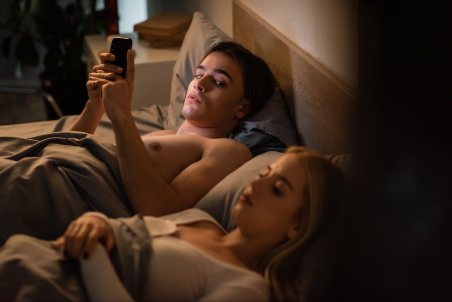 Mann heimlich am Smartphone, Frau neben ihm im Bett