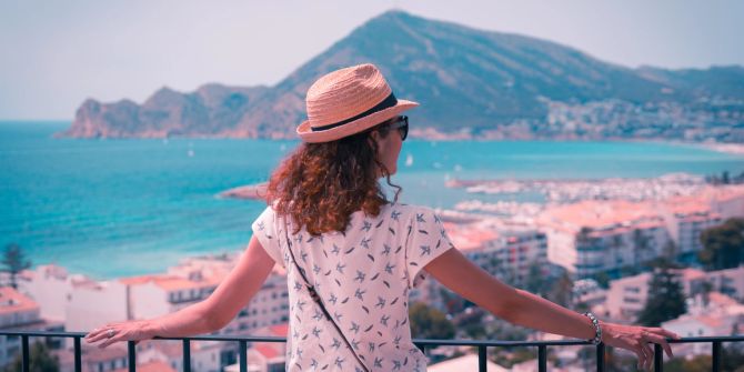 Frau blickt alleine auf eine Stadt und das Meer, Single Reisen