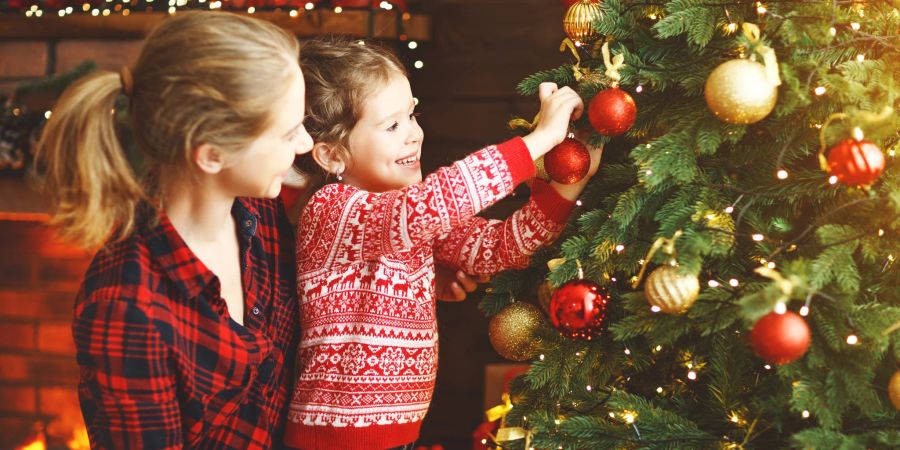 Eine Frau schmückt gemeinsam mit einem kleinen Mädchen liebevoll ihren Weihnachtsbaum.