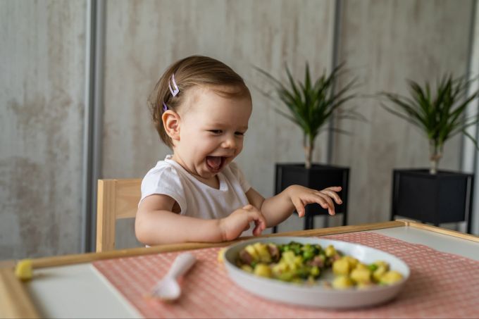 Kinder benötigen Zeit, um sich für neues Essen zu begeistern ‒ und nicht alles werden sie mögen, was auch okay ist. Fröhliches Kind schaut auf einen Teller mit Gemüse