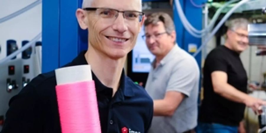 Robert Hufenus vor der Maschine, die als Weltneuheit Übertragungskabel mit Flüssigkern herstellt. Die Spule, die er in der Hand hält, ist nicht nur rosa, damit sie schick aussieht: Die Farbe erlaubt, die Dehnung der Faser zu messen. Das erweitert die Einsatzmöglichkeiten erheblich (Pressebild).