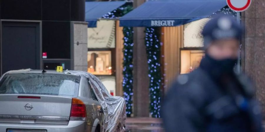 Polizeibeamte sichern nach einem Überfall den Tatort mit dem Tatfahrzeug vor einer Filiale der Schweizer Luxusuhrenmanufaktur Breguet hinter der Königsallee in Düsseldorf. Foto: Rolf Vennenbernd/dpa