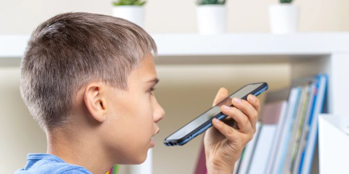 Ob lange Bildschirmzeiten oder Cybermobbing, Smartphones haben auch Nachteile. Junge spricht ins Handy