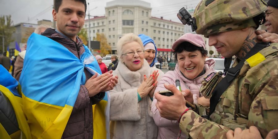 Einwohner von Cherson applaudieren den Soldaten, während ein ukrainischer Soldat seine Wünsche für einen in die Nationalflagge eingewickelten Mann schreibt. Foto: Efrem Lukatsky/AP/dpa