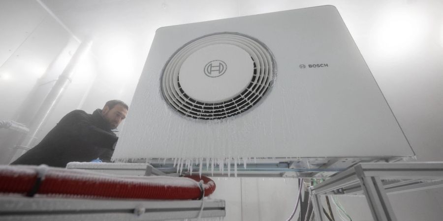 Ein Mitarbeiter der Bosch Thermotechnik GmbH öffnet in einer Klimakammer das Gehäuse einer Bosch-Wärmepumpe.