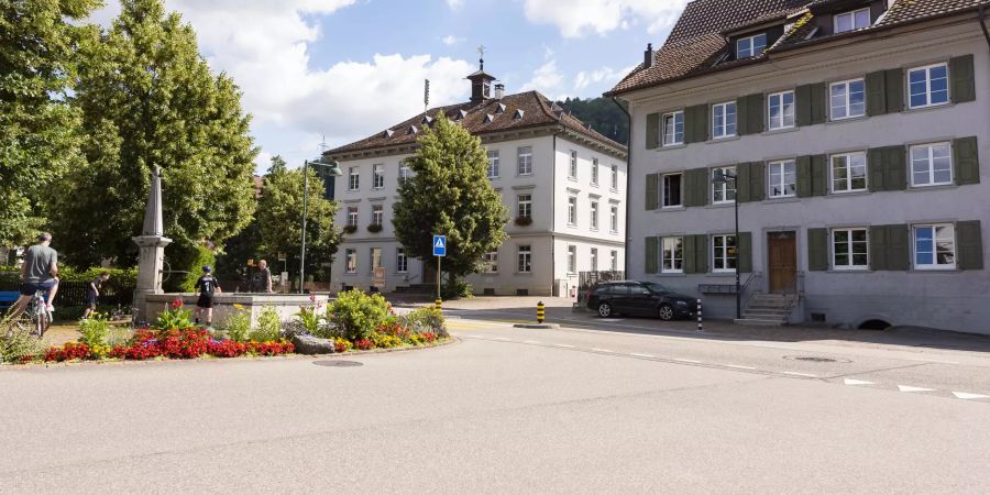 Der Dorfbrunnen mit dem Schulhaus an der Hauptstrasse in Ormalingen.