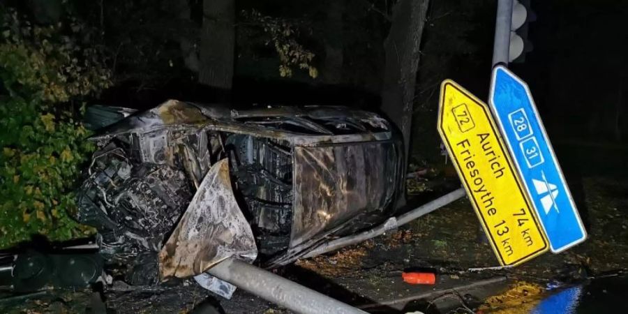 Das ausgebrannte Auto liegt auf der Seite hinter einem umgeknickten Strassenschild und einem auf dem Boden liegenden Ampelmast. Foto: -/Nord-West-Media TV/dpa