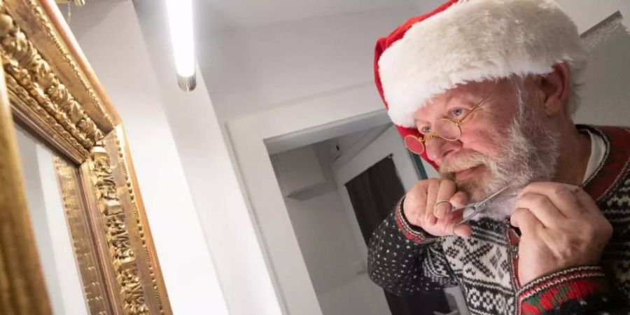 Willi Dahmen, professioneller Weihnachtsmann-Darsteller, kürzt seinen Bart. Die Corona-Pandemie bringt in diesem Jahr aber Hunderte Miet-Weihnachtsmänner in Deutschland um ihren Job. Foto: Julian Stratenschulte/dpa