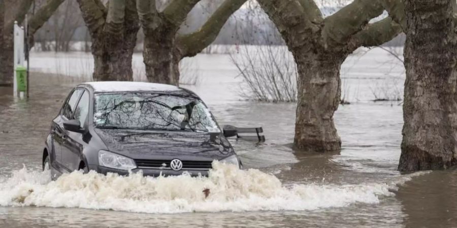 Ein Autofahrer steuert in Rüdesheim am Rhein seinen Wagen über eine vom Hochwasser überflutete Strasse. Foto: Boris Roessler/dpa