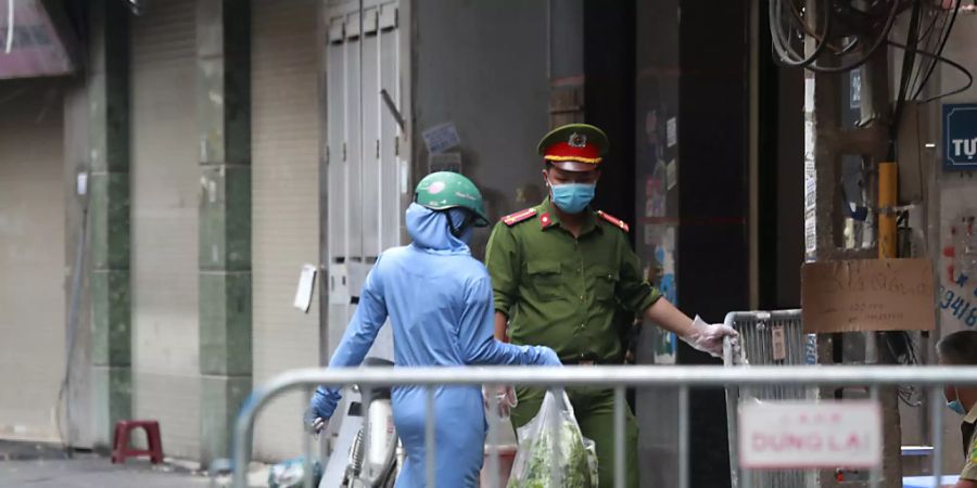 ARCHIV - Eine Frau geht vor einem Supermarkt in Hanoi an einem Polizisten mit Mundschutz vorbei. Foto: Hau Dinh/AP/dpa