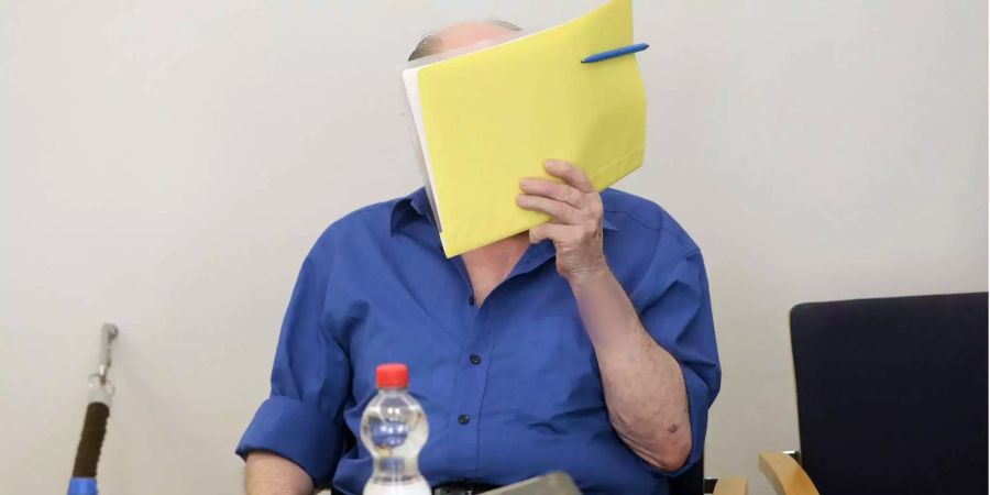 Der Angeklagte sitzt im Gerichtssaal und verdeckt sein Gesicht. Sechs Monate nach den tödlichen Schüssen auf eine Rechtsanwältin in Waren an der Müritz gesteht der 80-Jährige vor Gericht.