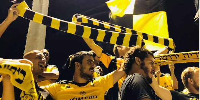 Die Fussballfans von Beitar Nordia singen und halten die Fanschals hoch. Die Fussballfans von Beitar Nordia singen und halten die Fanschals hoch.