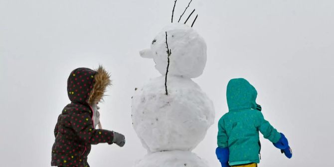 Zwei Kinder bauen mit dem Haufen Schnee einen Schneemann.