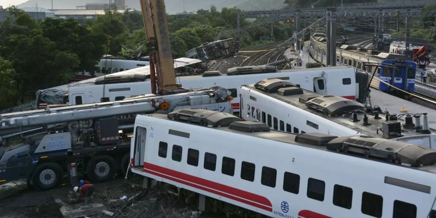 Ein Zug (r) passiert entgleiste Zugwaggons, die neben den Gleisen stehen und liegen.