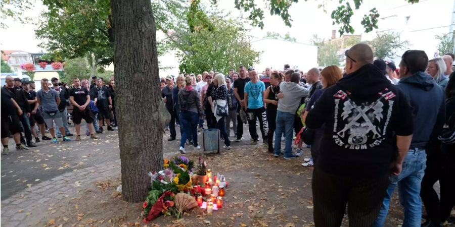 Menschen stehen vor Blumen und Kerzen an einem Baum auf einem Spielplatz, in dessen Nähe ein 22-Jähriger bei einem Streit zwischen zwei Männergruppen ums Leben gekommen ist.