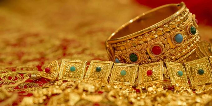 Bahrainischer Goldschmuck liegt auf einem goldbesticktem roten Tuch. Bahrainischer Goldschmuck liegt auf einem goldbesticktem roten Tuch.