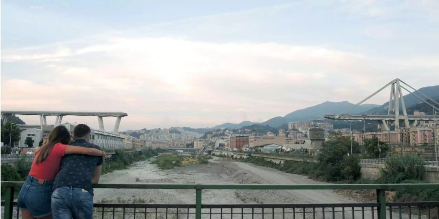 Ein Paar steht auf einer Brücke, von der man auf die Überreste des Polcevera-Viadukts in Genua sehen kann.