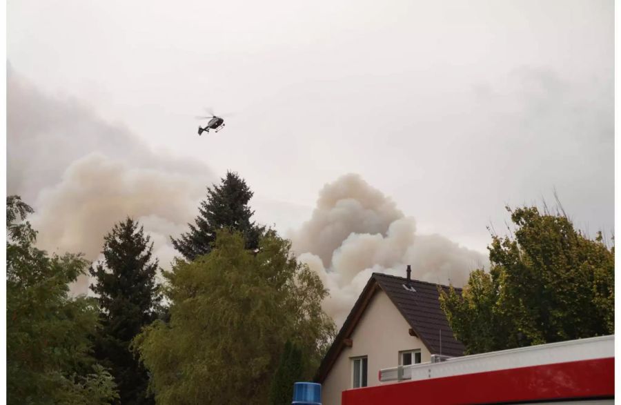 Rauch steigt in Frohnsdorf neben einem Haus auf, über dem ein Helikopter schwebt.