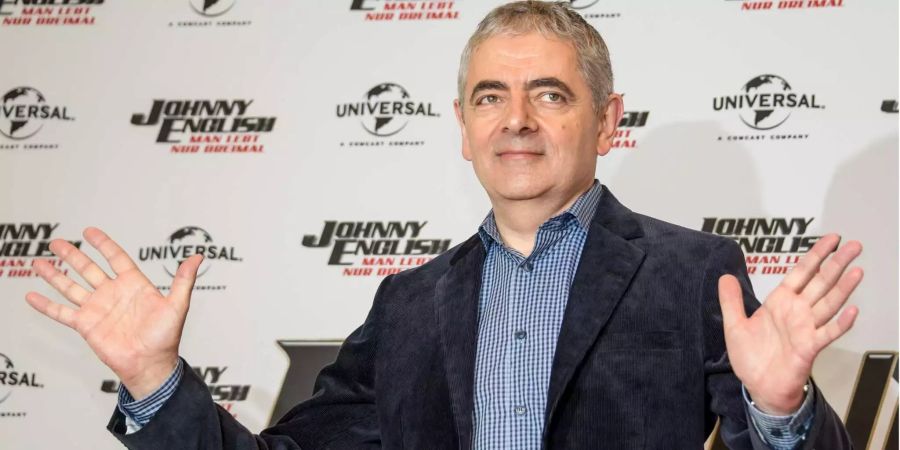 Rowan Atkinson, britischer Schauspieler, steht vor einer Wand die den Schriftzug seines neuen Films «Johnny English - Man lebt nur dreimal» trägt.