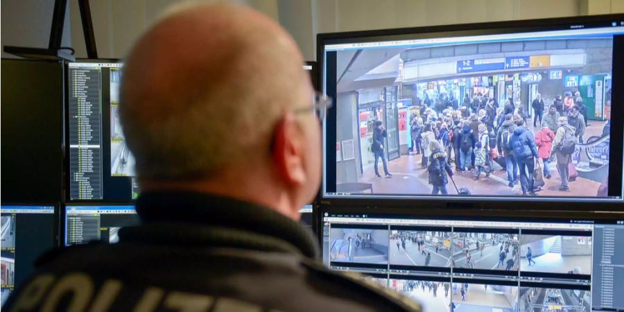 Ein Beamter der deutschen Bundespolizei arbeitet an einem Videoarbeitsplatz, auf dessen Monitoren Live-Bilder von Überwachungskameras am Hamburger Hauptbahnhof zu sehen sind.