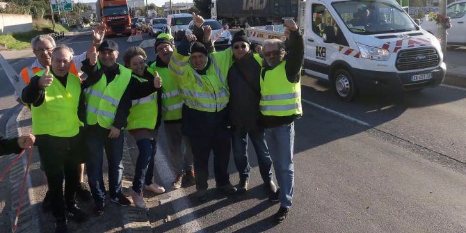 Demonstranten mit gelben Westen lachen bei einem Protest gegen die Steuererhöhungen für Benzin und Diesel an einer Kreuzung.