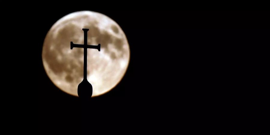 Ein Kreuz einer Kirche vor dem Vollmond.