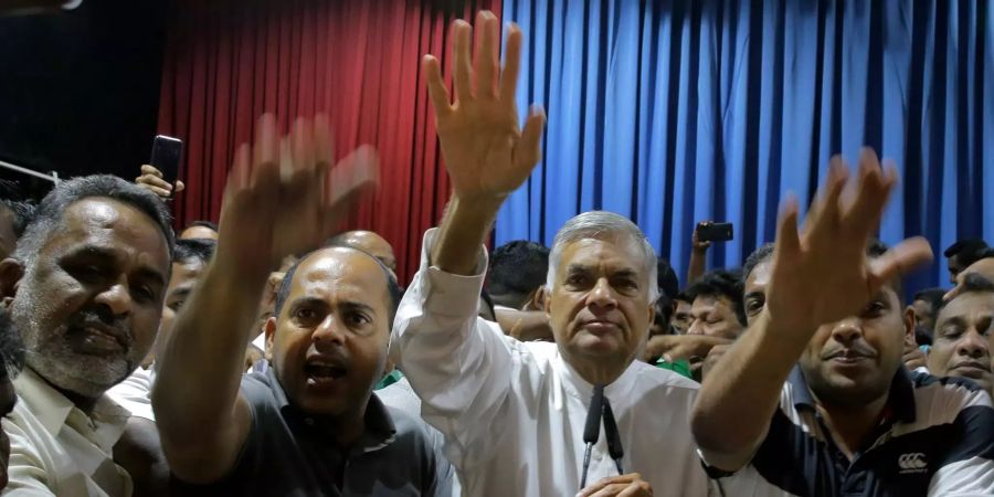 Ranil Wickremesinghe (M), entlassener Premierminister von Sri Lanka, hebt gemeinsam mit Unterstützern die Hand nach einer Pressekonferenz in seiner Residenz.