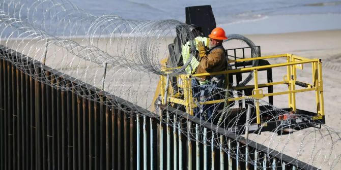 Ein Handwerker auf der US-Amerikanischen Seite der Grenze bei Tijuana bringt Stacheldraht auf dem Grenzzaun an.