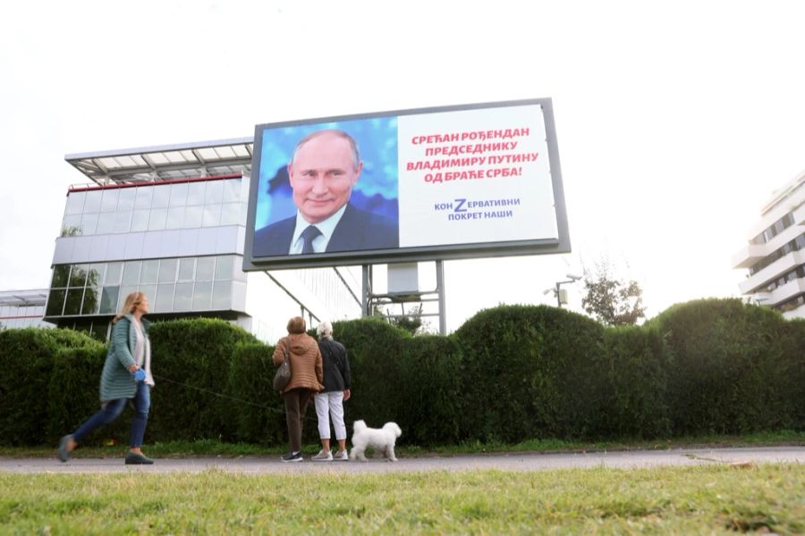 Menschen betrachten ein Plakat, das den russischen Präsidenten Wladimir Putin zeigt.