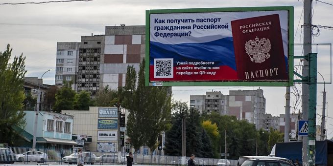 Menschen überqueren eine Strasse mit einem Plakat mit der Aufschrift «Wie man den Pass eines russischen Bürgers bekommt» vor dem Scheinreferendum in der von den Russen kontrollierten Volksrepublik Luhansk. Foto: Uncredited/AP/dpa referenden