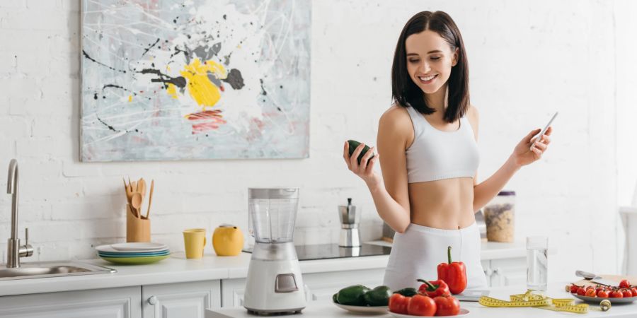 sportliche frau schaut lächelnd auf avocado, küche