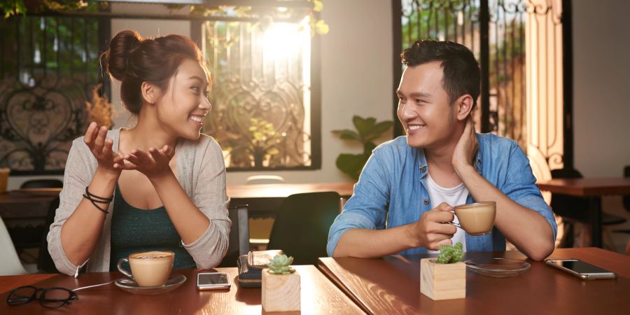 asiatische frau lächelt mann an cafétisch an, sonne scheint durch fenster